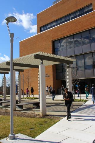 Male student wearing black zip jacket and black pants walking in front of a group of students walking in front of the Grace Jacobs Building on Coppin State University's campus