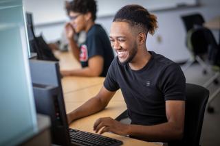 A smiling male student types on a computer