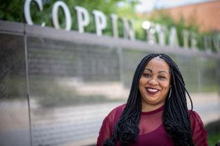 A female student with braids smiles and stands by the Coppin State University wall
