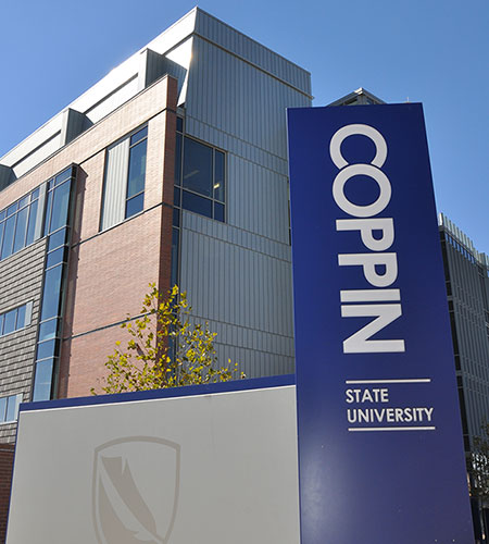 Side view of the Science and Technology Center behind a royal blue sign with Coppin State University in large white writing