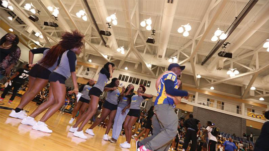 Group of brown skins students in black shorts, grey tshirts, and white sneakers standing on the basketball court