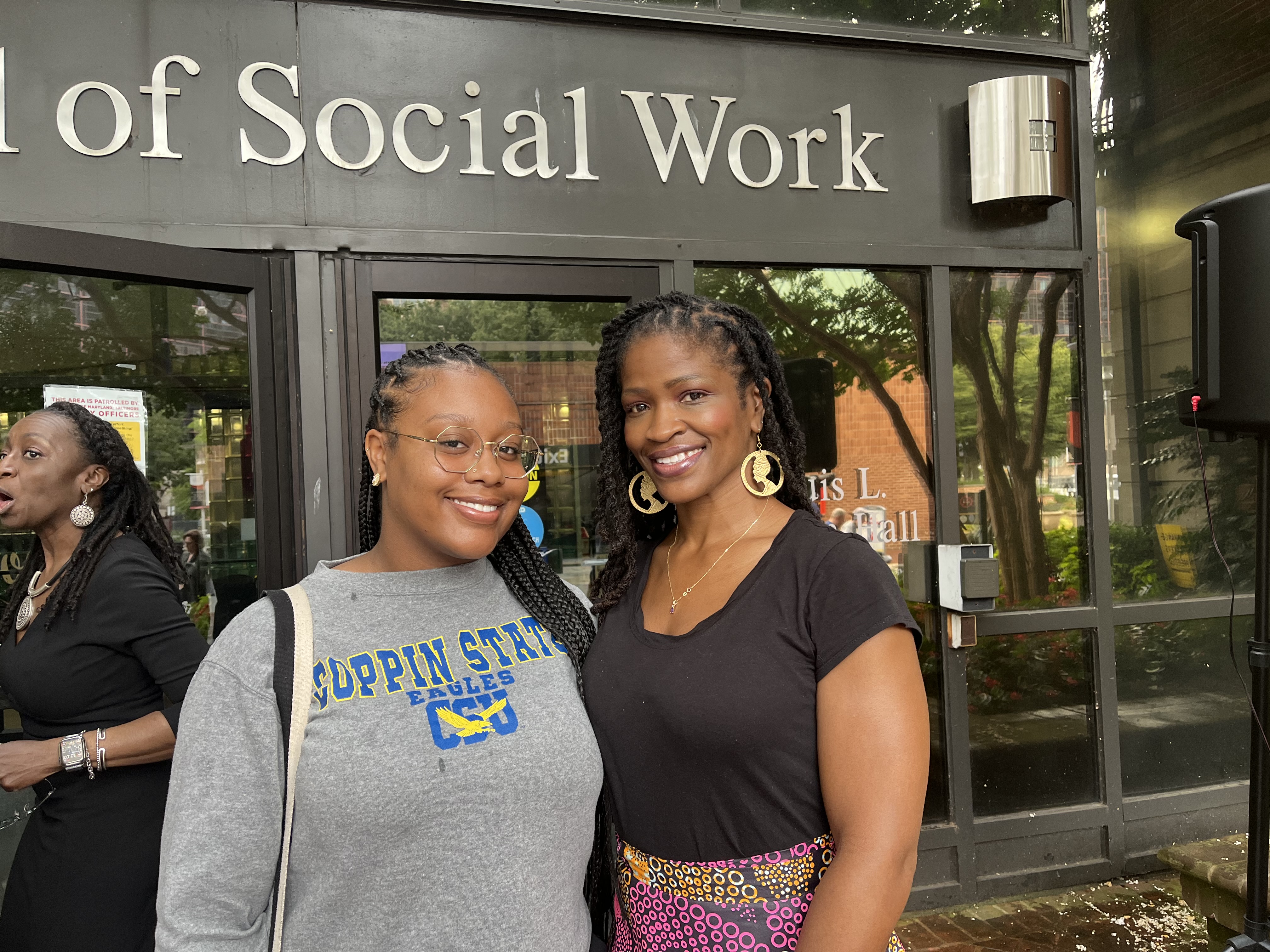 A young woman on the right wearing a Coppin State sweatshirt smiles beside an older woman on right with braids