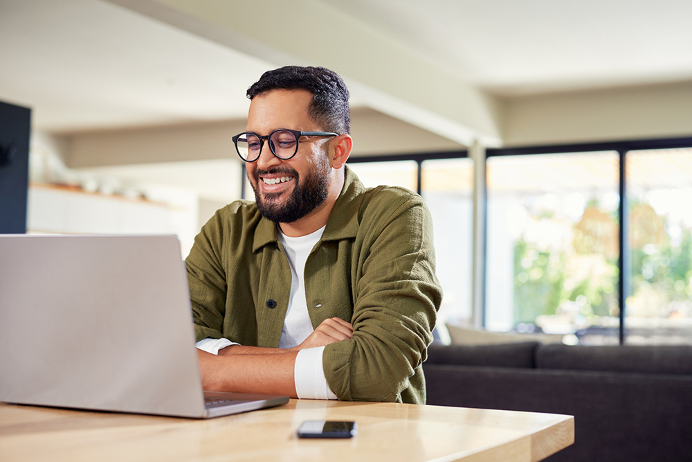 Smiling young man sitting at home while using laptop