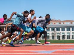 Group of brown skin men wearing different color shirts, shorts, and sneakers while running the track at Coppin State University's Physical Education Complex
