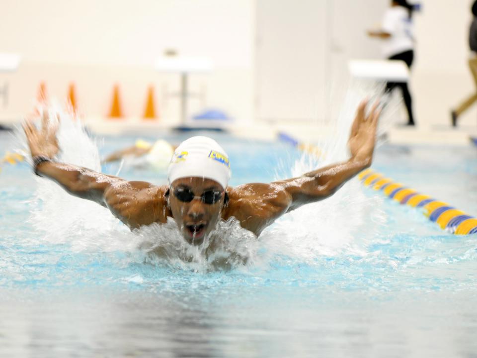 Close up of brown skin swimmer wearing white swimmers cap and swimming googles in the middle of a breast stroke in the pool of Coppin State University's Physical Education Complex 