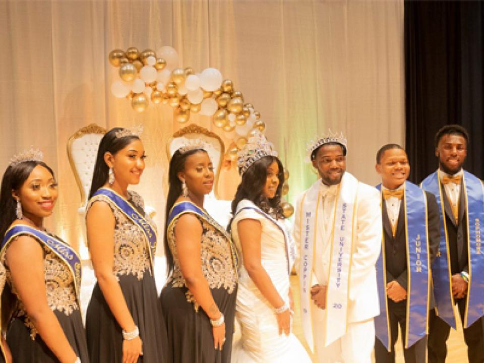 Posed picture of 9 Coppin students dressed formally while wearing their royal court regalia