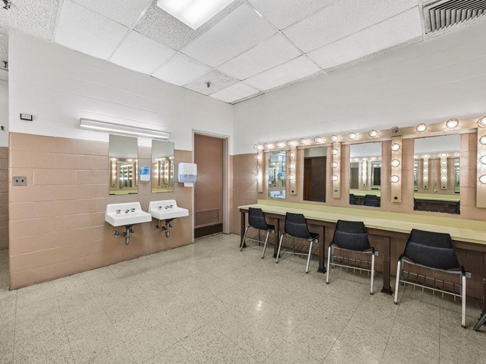 Dressing Room with numerous seated, lighted mirrored vanities with two sinks.