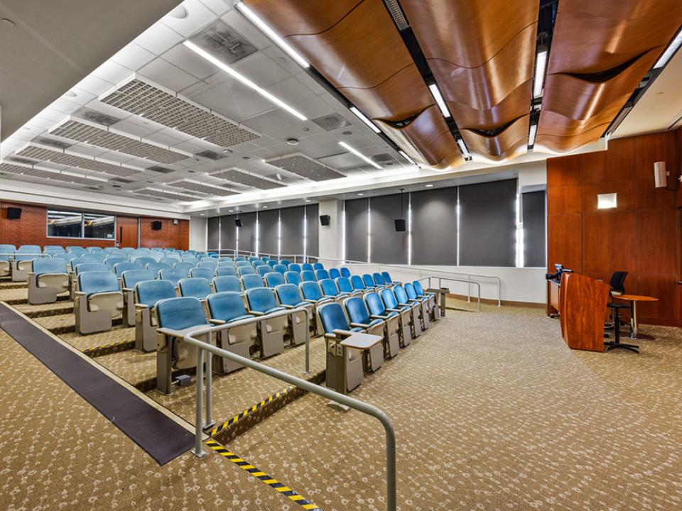 Large lecture room with 10 rows of tiered seating and wood ceiling acoustic paneling