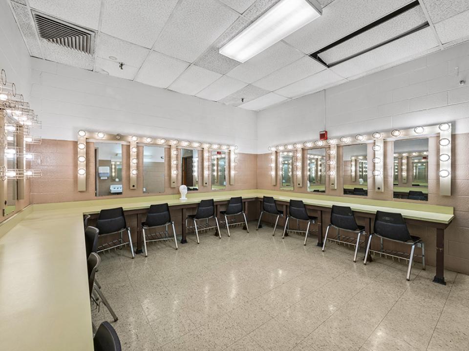 Dressing Room with numerous seated, lighted mirrored vanities with two sinks.