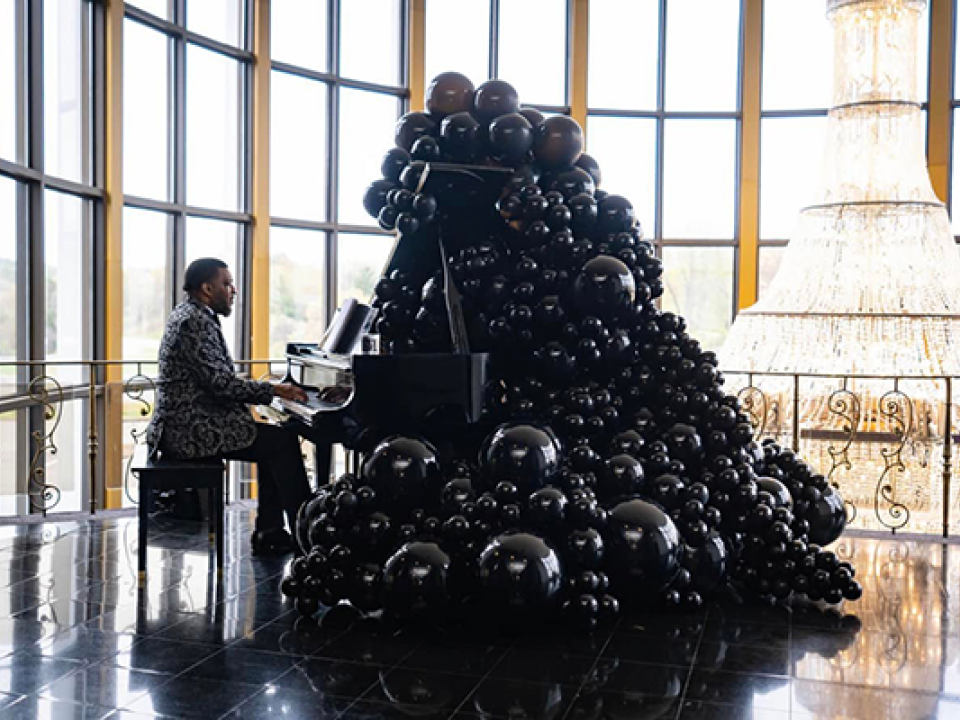 Stock image of man playing piano in fancy room with a black ballon mountain and chandelier.