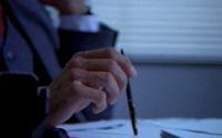 Close up of the right hand of a person in a business suit holding a pen