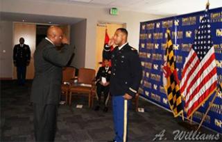 A Coppin State University ROTC Cadet saluting another officer while standing in front of the US flag and Maryland State flag during a Commissioning Ceremony