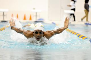 Close up of brown skin swimmer wearing white swimmers cap and swimming googles in the middle of a breast stroke in the pool of Coppin State University's Physical Education Complex 
