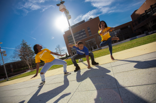 Students wearing blue and yellow Coppin shirts make dramatic poses on a sunny day