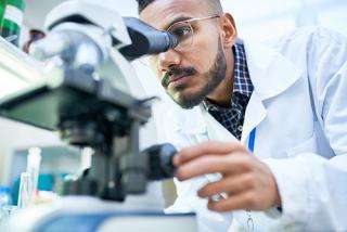 Male student looking in microscope while working on research in chemistry laboratory.
