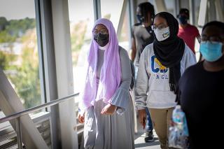 Students in masks walk across the campus bridge