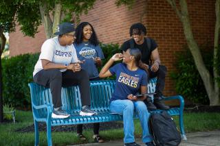 A group of four students chatting on a blue bench on Coppin's campus
