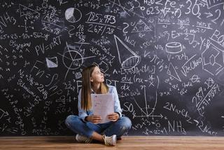 A female student sitting in front of big blackboard with math problems.
