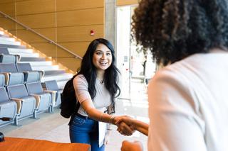 Female college student smiles as she shakes hands with a female professor. 