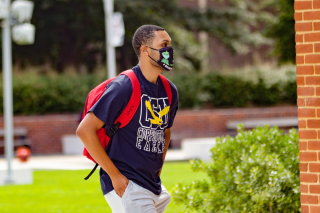 Male Coppin student walking on campus wearing CSU shirt.