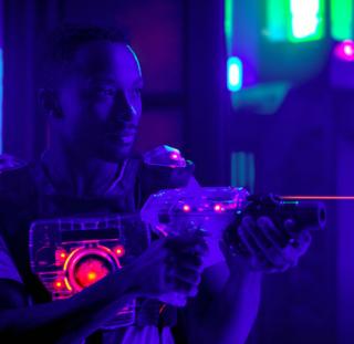 laser tag player holding gun shooting light in black light labyrinth