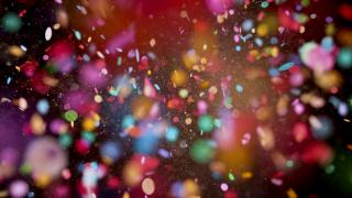 Close-up of multi coloured confetti flying mid-air against black background.