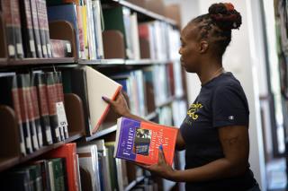 Photo of a Coppin student pulling books in the Parlett L. Moore Library
